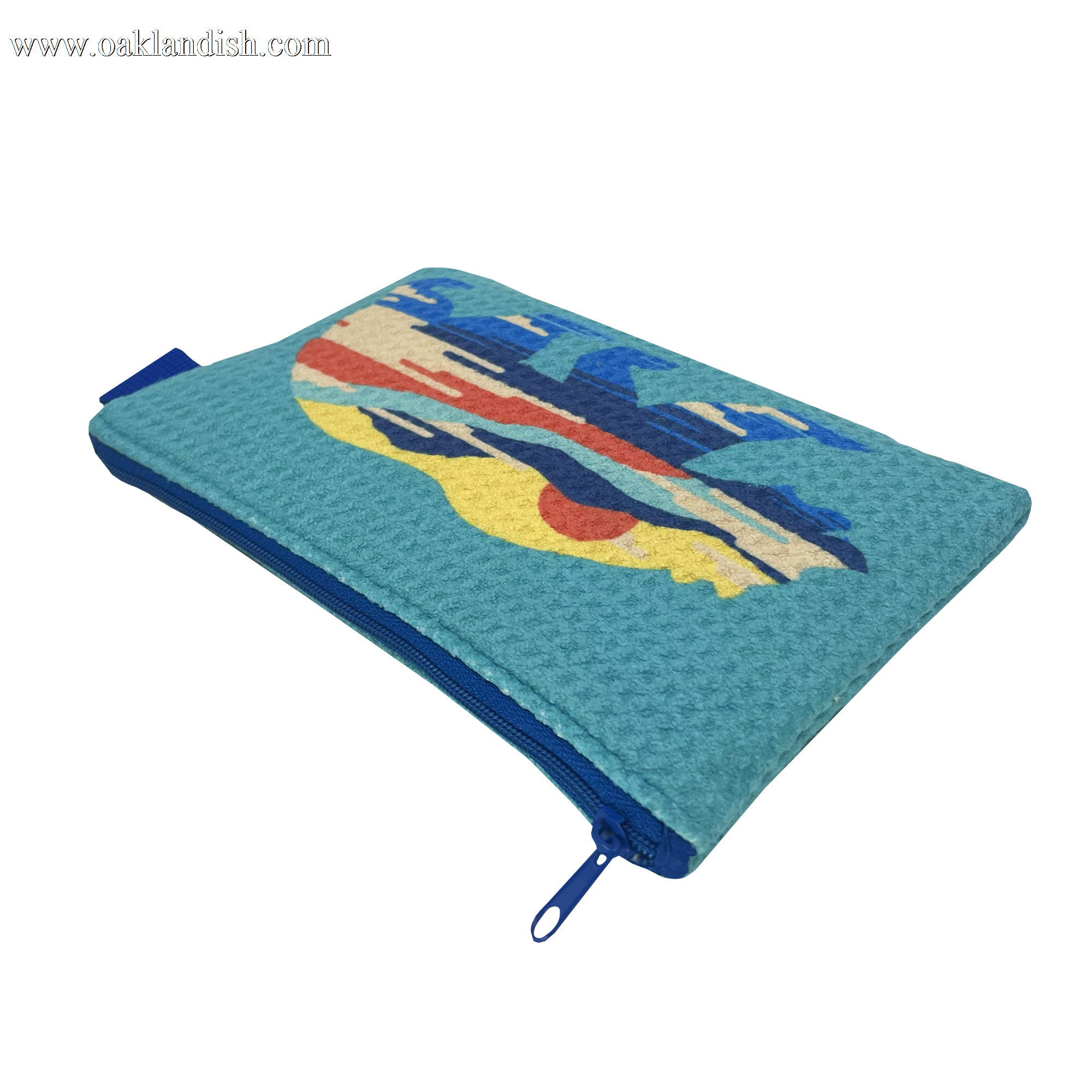 The Sunset Bear Pouch by Oaklandish is a rectangular, turquoise zip pouch that features a vibrant, abstract design on one side. Made from waffle weave fabric, it has a blue zipper extending to one side and is finished with a small blue pull tab. The striking design includes various shapes in blue, red, and beige hues.