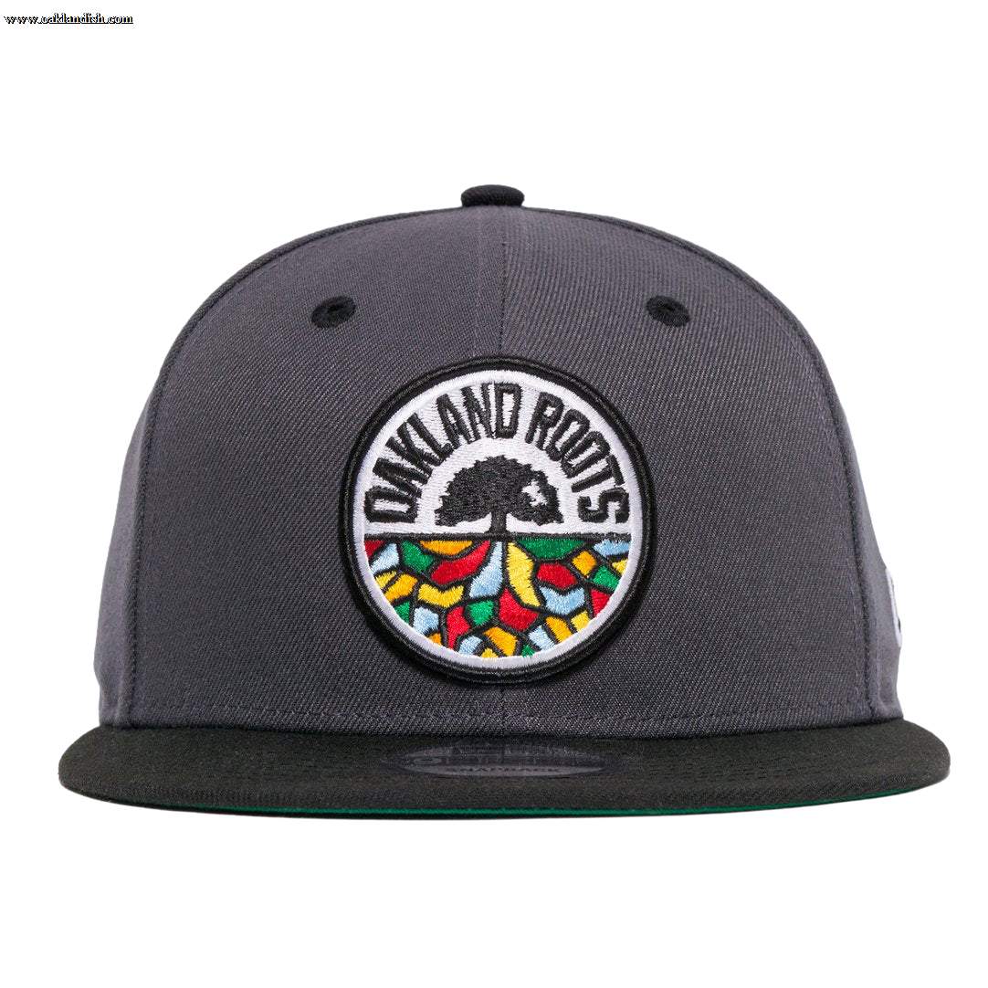 The New Era Oakland Roots SC 59FIFTY Fitted cap, in dark grey, showcases an intricately embroidered logo on the front featuring a black tree with spreading roots. Surrounding the tree is the bold text "OAKLAND ROOTS," accented by colorful shapes in red, yellow, green, and blue that symbolize the foundational pride of this distinguished sports club.