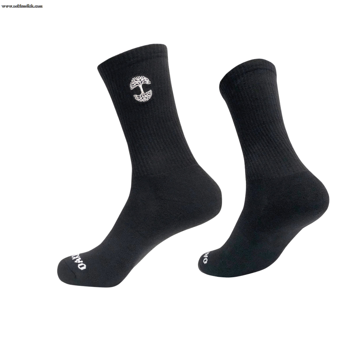 A pair of black crew socks, with one sock slightly elevated and angled to the side. The Embroidered Logo Socks feature a small, white, vertical emblem resembling a tree on the upper part and white text "OAKPO" near the toes. These Oaklandish socks come in adult sizes, boasting a ribbed texture on top and smooth finish below.