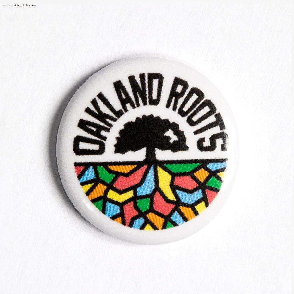 The Oakland Roots SC Pin by Oakland Roots SC features the bold black text "OAKLAND ROOTS" at the top, representing the Oakland Roots Sports Club. Below, a stylized tree outline is set against a vibrant background of colorful mosaic patterns in yellow, red, green, and blue hues.