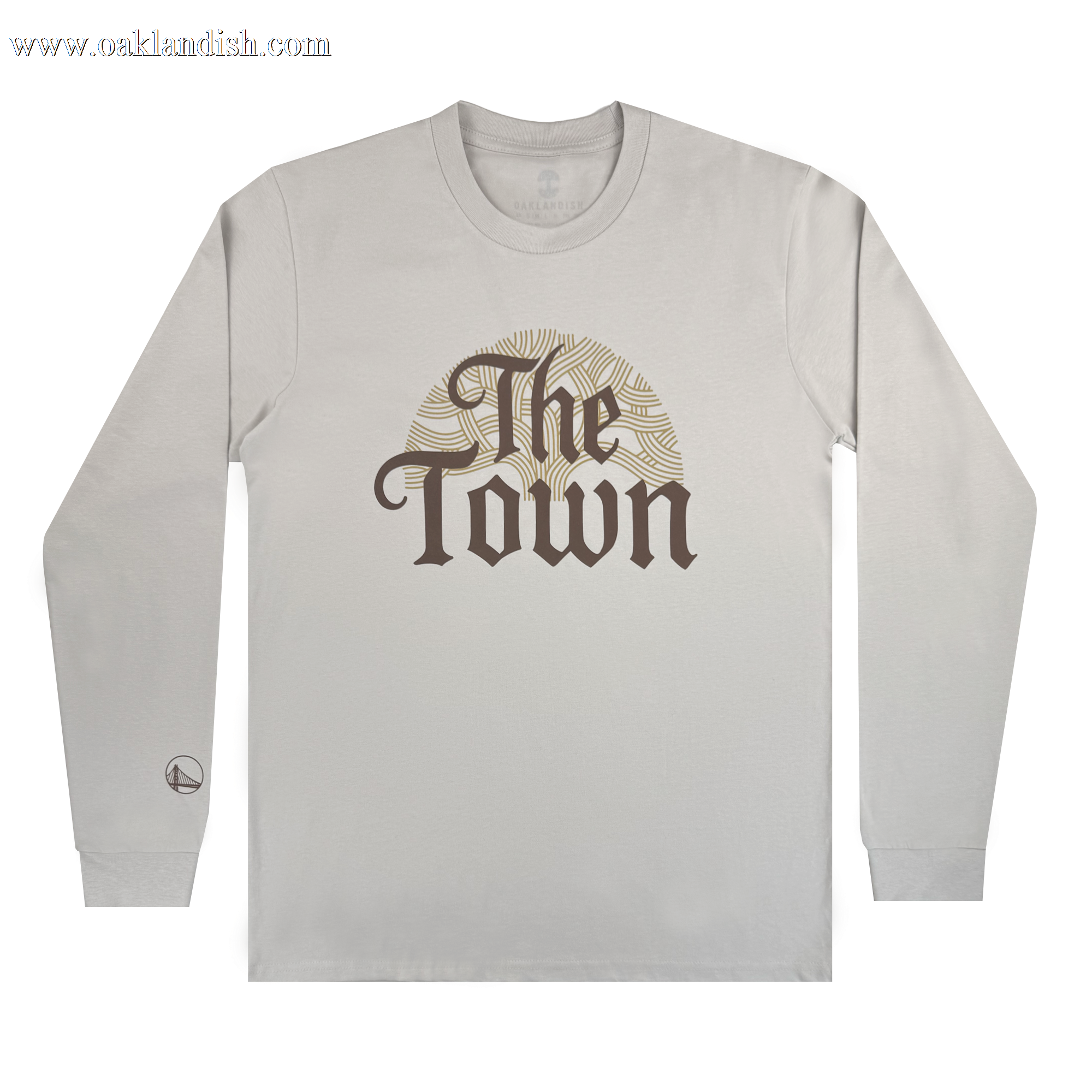 A light gray long-sleeve Pirate Black-Letter LS Tee by Other, featuring "The Town" in bold, ornate brown letters across the chest over a circular gold sunburst design. A small logo appears near the left sleeve cuff. The shirt is laid flat on a plain white background.
