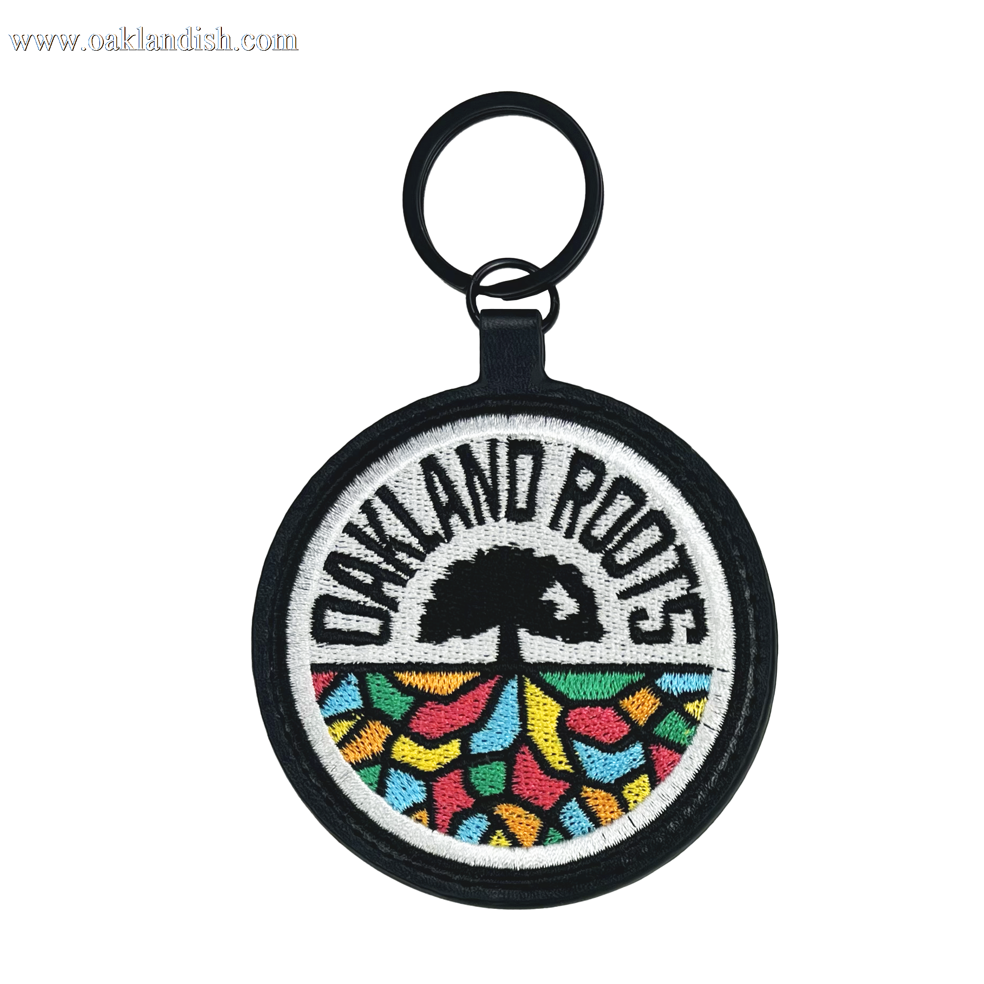 Introducing the Oakland Roots SC Logo Keychain from Oakland Roots SC! This circular keychain proudly showcases the Oakland Roots logo, featuring "OAKLAND ROOTS" in bold black text at the top, a striking black tree silhouette in the center, and vibrant abstract shapes resembling the ground beneath. Celebrate your favorite sports club with this stylish accessory that also supports social good initiatives.