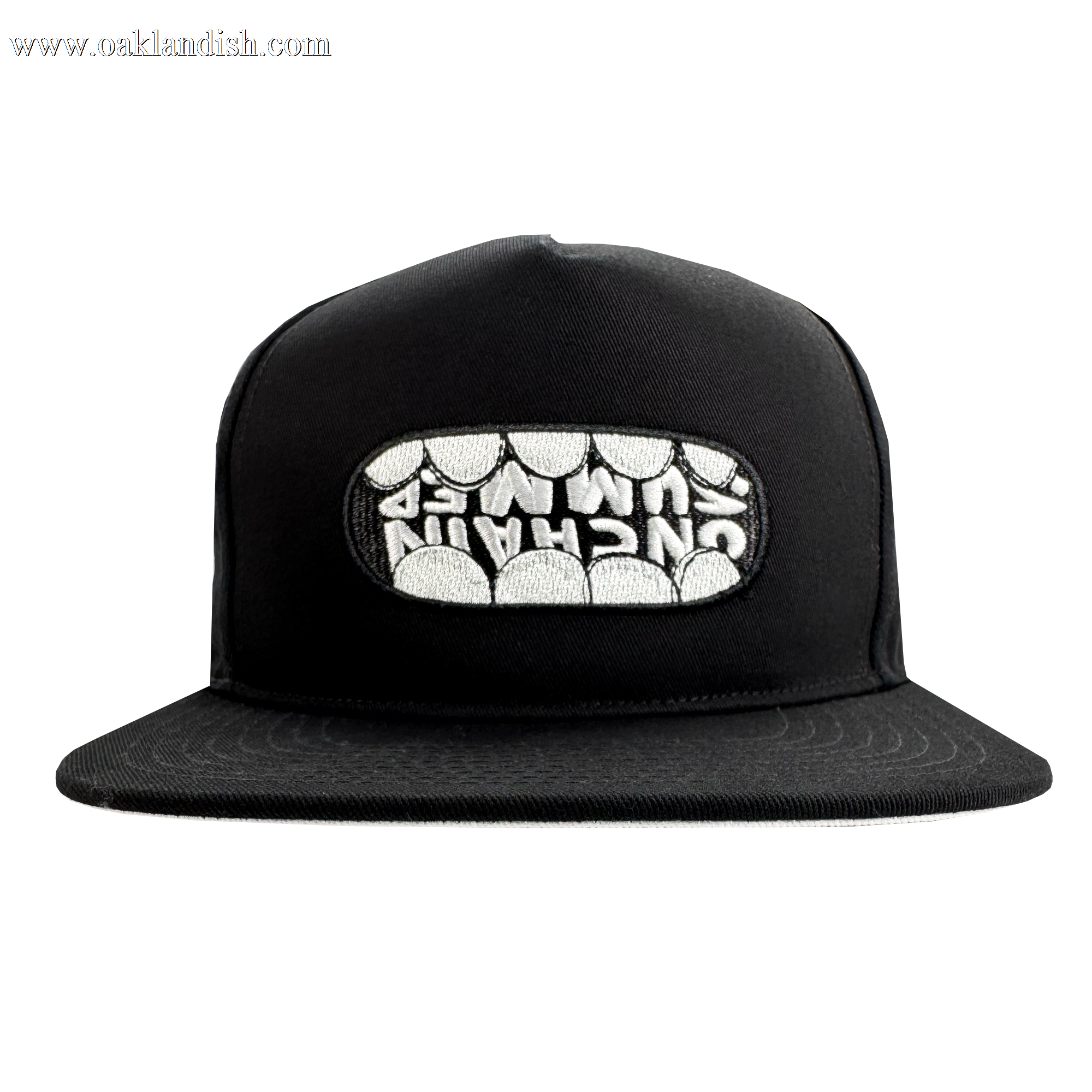 The OG Snapback Hat by Supported Brands is a black adjustable snapback featuring a front embroidered patch where stylized white teeth spell “UNCHAIN” across the upper row. Photo shows the hat on a plain white background.