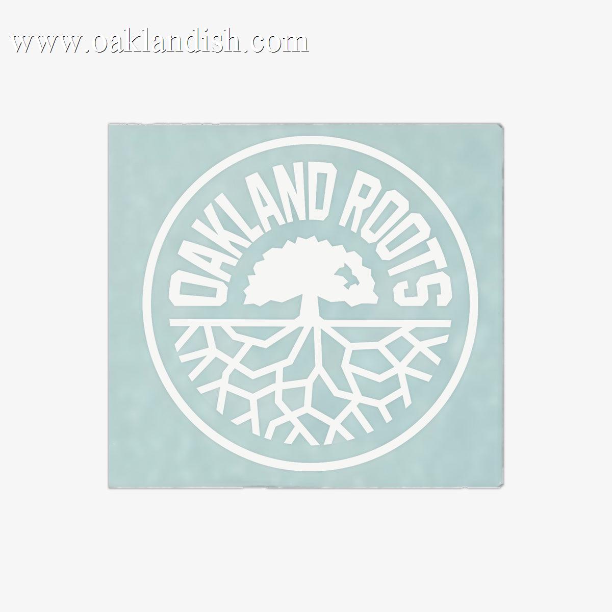 The Oakland Roots SC Decal - 6" features a pale blue-green background with a white circular logo. "OAKLAND ROOTS" is written in all caps along the top edge inside the circle, while a simplified tree with visible roots is centered within it, symbolizing Oakland Roots Sports Club's deep connection with its community. This decal is perfect for adorning your window!