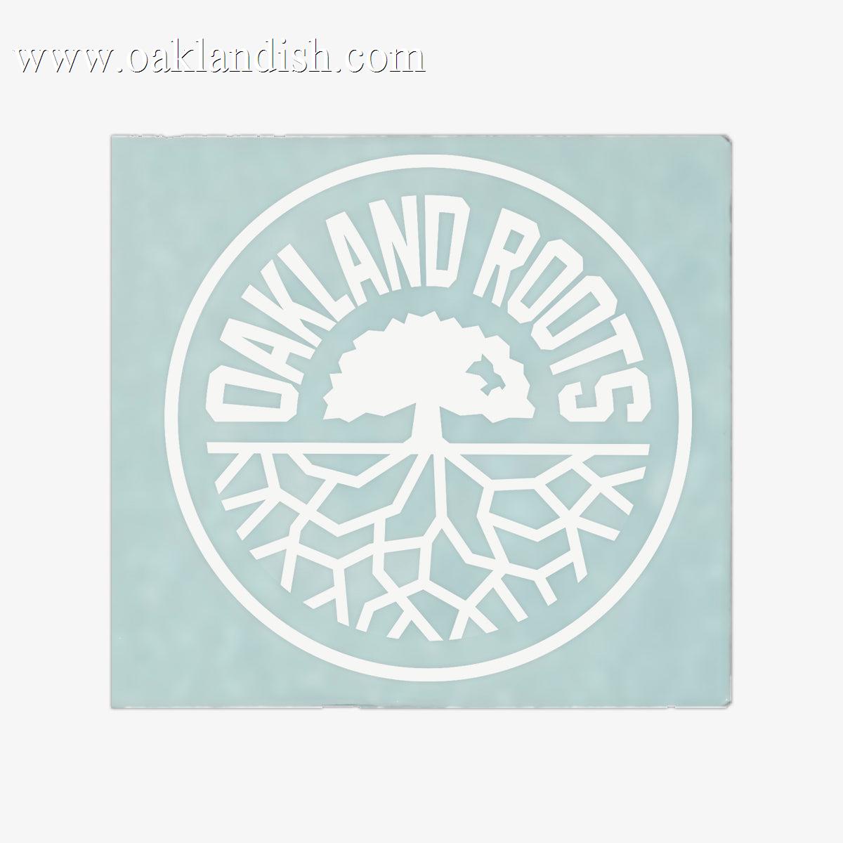 Introducing the Oakland Roots SC Decal - 8", featuring a circular logo with a light teal background. Inside the circle is a striking white illustration of a tree with roots extending outward. Bold, white capital letters spelling "OAKLAND ROOTS" curve along the top inside of the circle, making it an ideal window decal for any sports club fan.