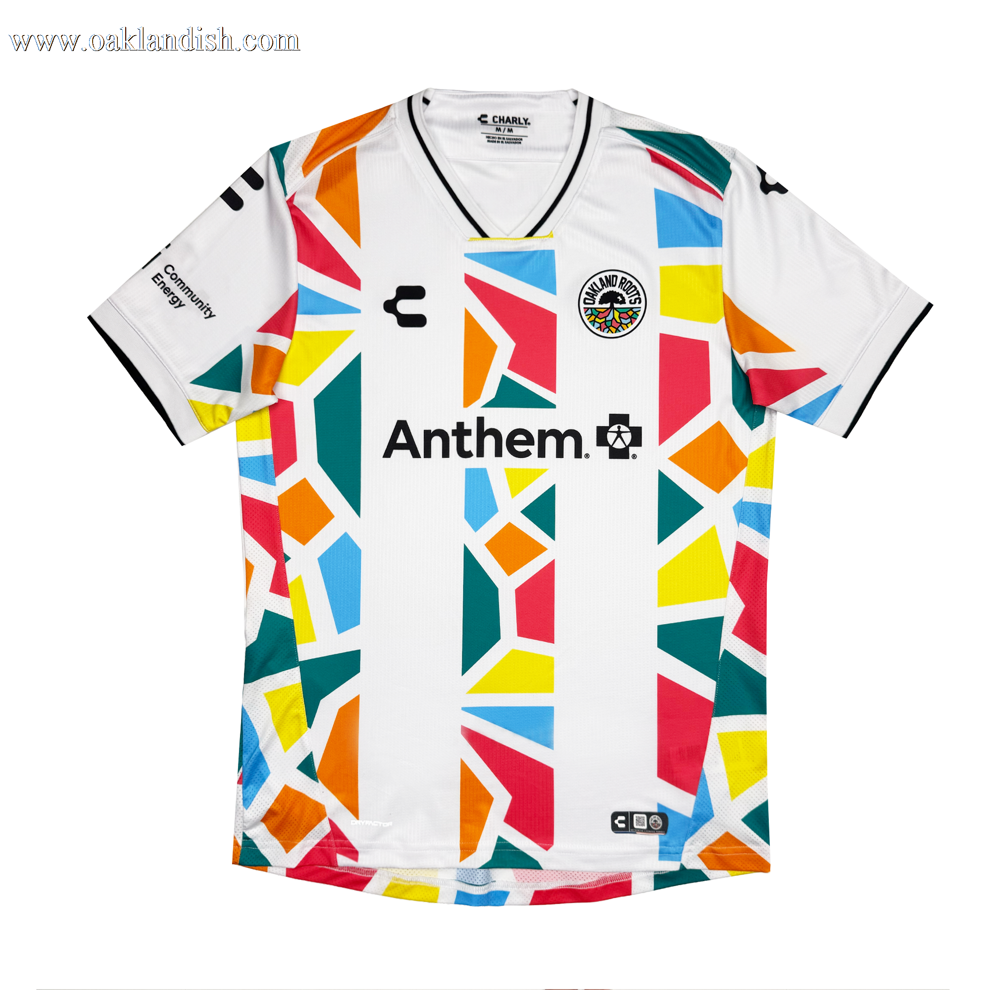 The Unisex Mosaic in Motion Kit by Oakland Roots SC is a white jersey with a black V-neck and sleeve trim, colorful geometric shapes, “Anthem.” and logo on the chest, an Oakland Roots 2026 rainbow badge, and sponsor logos on the sleeves.