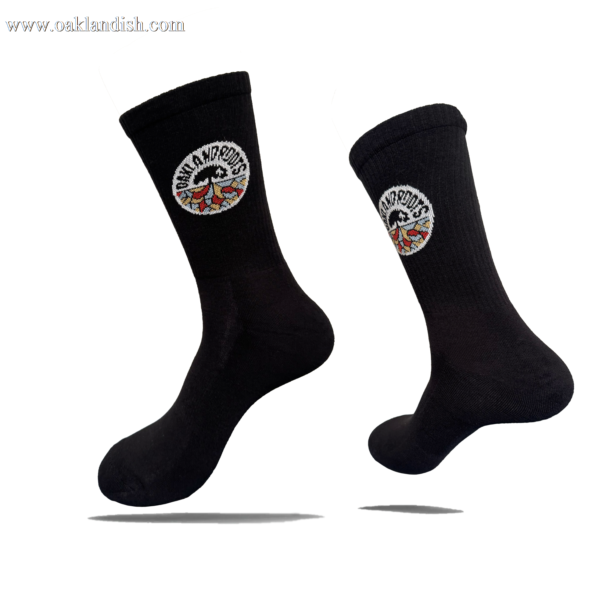 Two black cotton crew Roots SC Socks by Oakland Roots SC are shown against a white background. Each adult-sized sock features a round “NOMAD NOMADS” patch with colorful wings near the top and appears to float with shadows below.