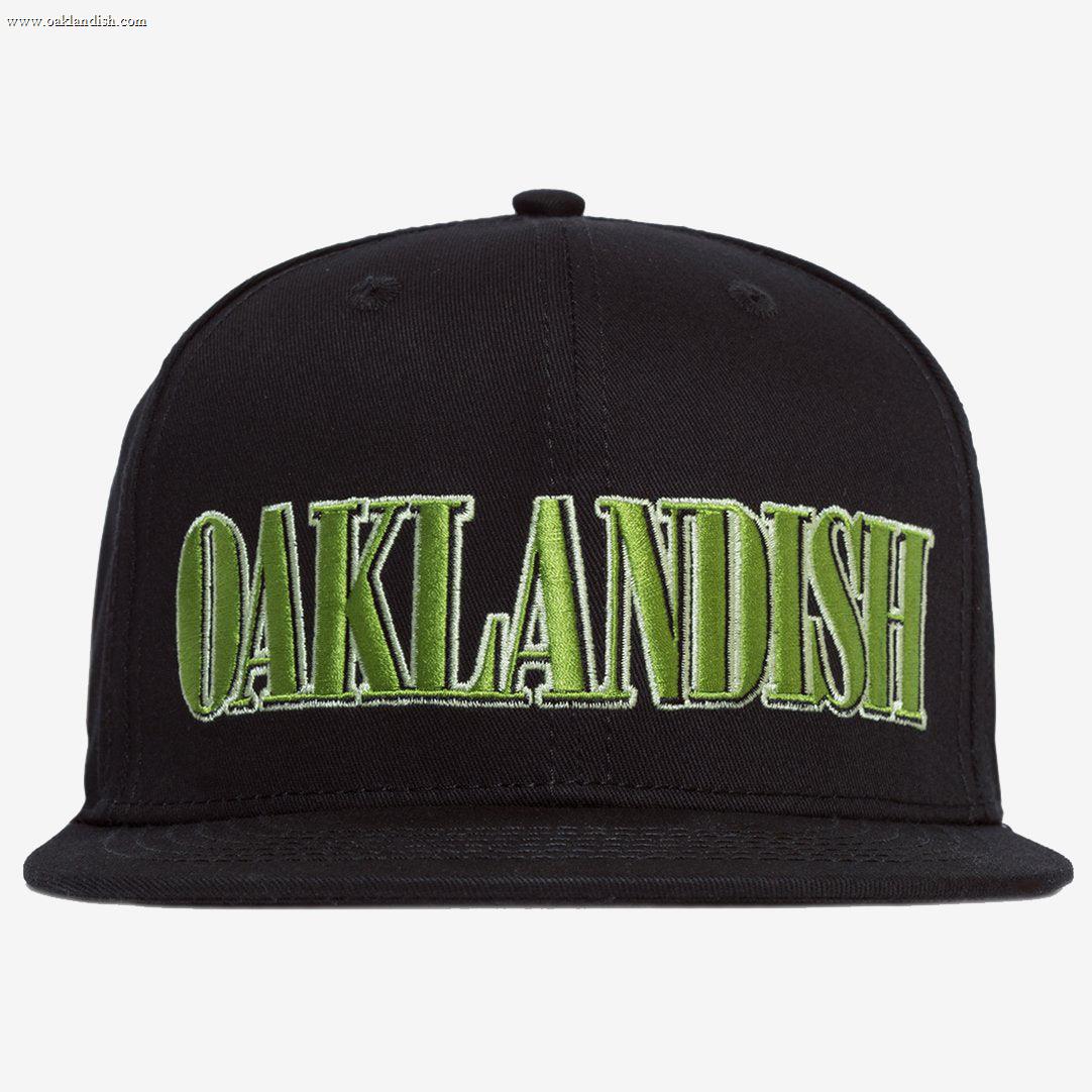 The Greenback Snapback by Oaklandish is a black cap with the word "OAKLANDISH" embroidered in large, green, capital letters on the front. This headwear features a flat brim and six ventilation eyelets, with two visible in this view.