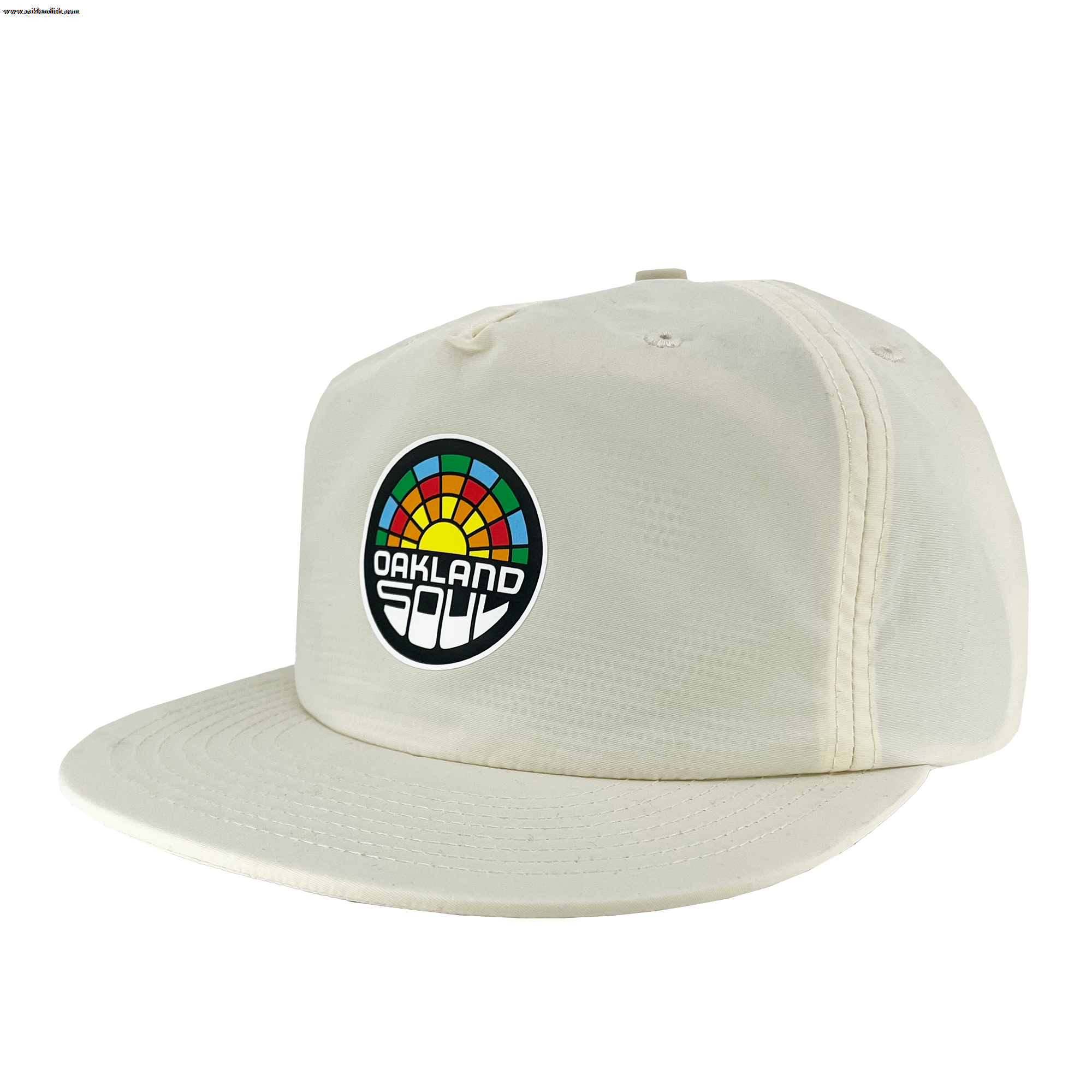 The Oakland Soul Surf Cap is a cream-colored baseball cap with a flat brim, featuring a colorful circular logo on the front. The logo displays a multicolored rainbow-like arc above the text "Oakland Soul," symbolizing the dynamic women's soccer team in the USL W-League, written in a bold, white, modern font against a black background.