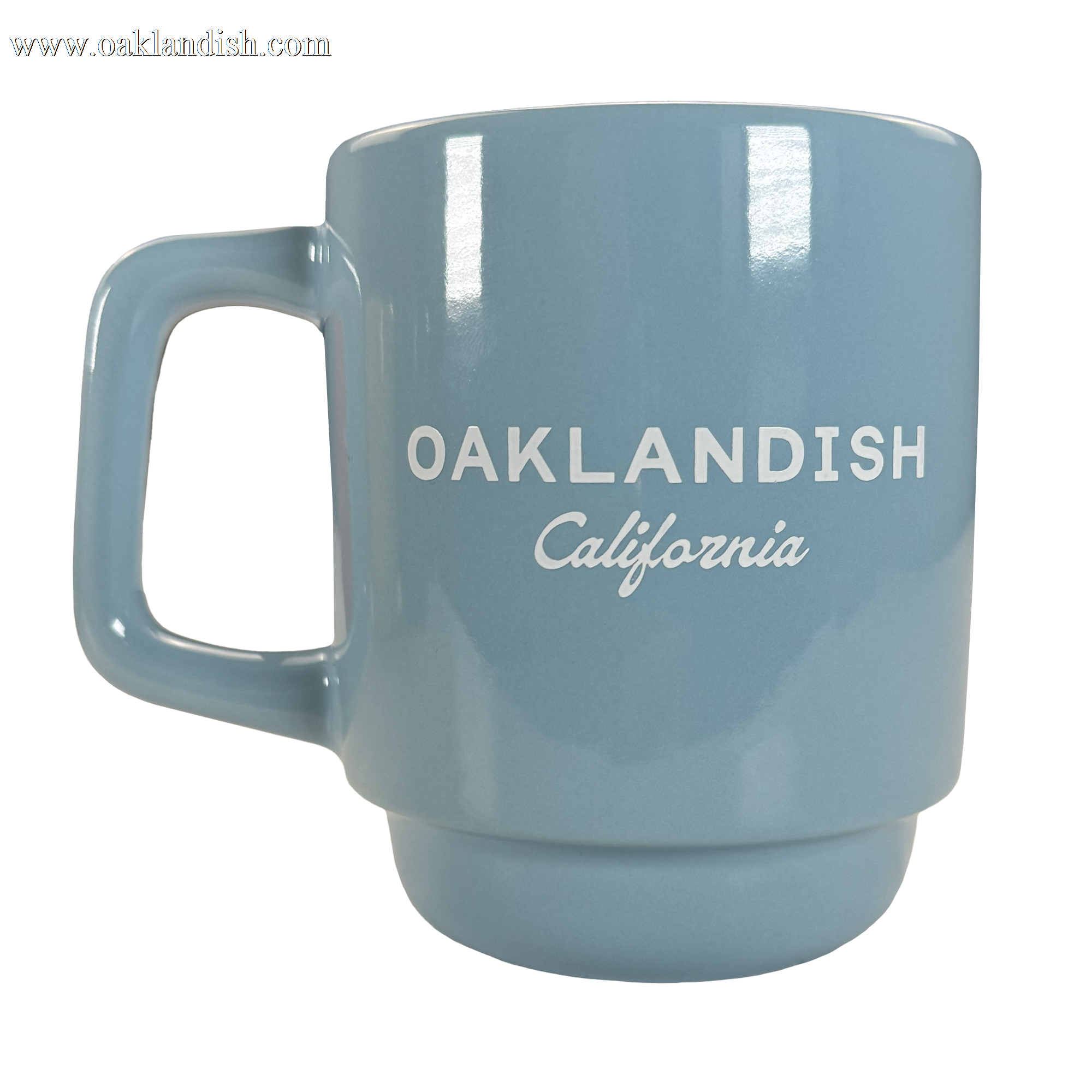 The Oaklandish Logo Stack Mug is a light blue ceramic mug with a squared handle, glossy finish, and white "OAKLANDISH California" text. This stackable drinkware piece is shown on a plain white background.