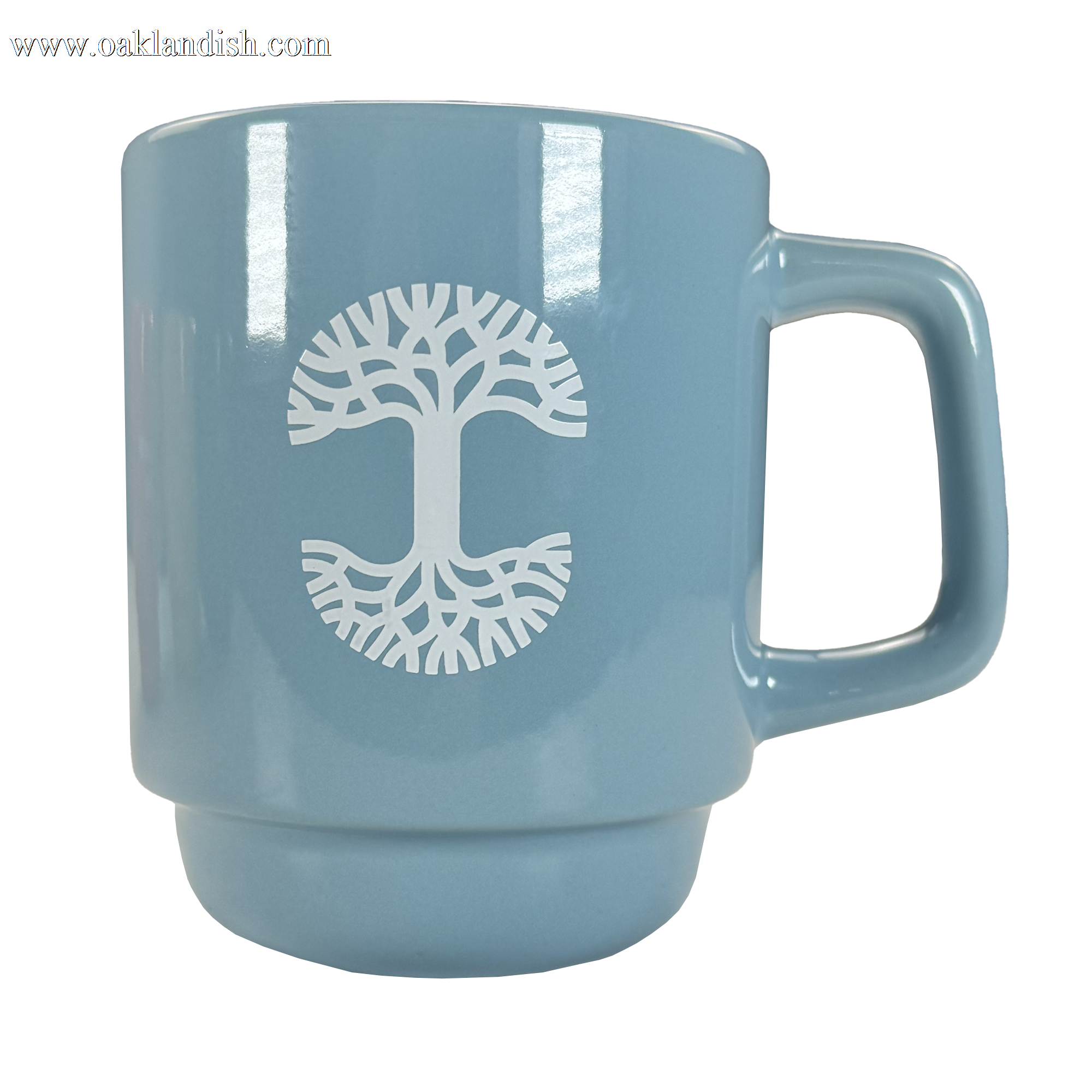 The Oaklandish Logo Stack Mug is a light blue ceramic mug with a large handle, featuring a white stylized tree logo with symmetrical branches and roots. It is photographed against a plain white background.