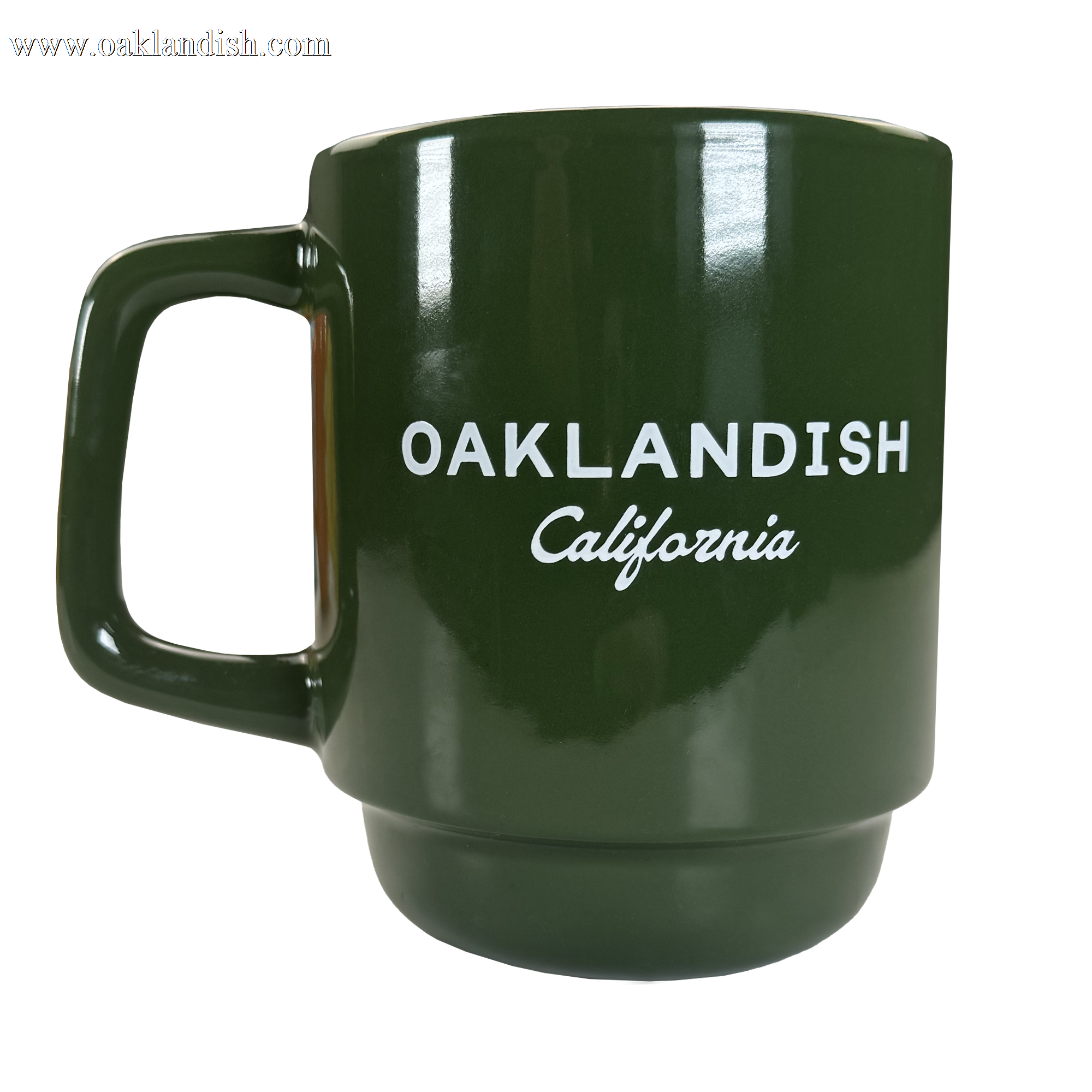 The Oaklandish Logo Stack Mug is a dark green ceramic mug with a large handle, featuring bold white "OAKLANDISH California" text on the front. Its modern design stands out against the plain background.