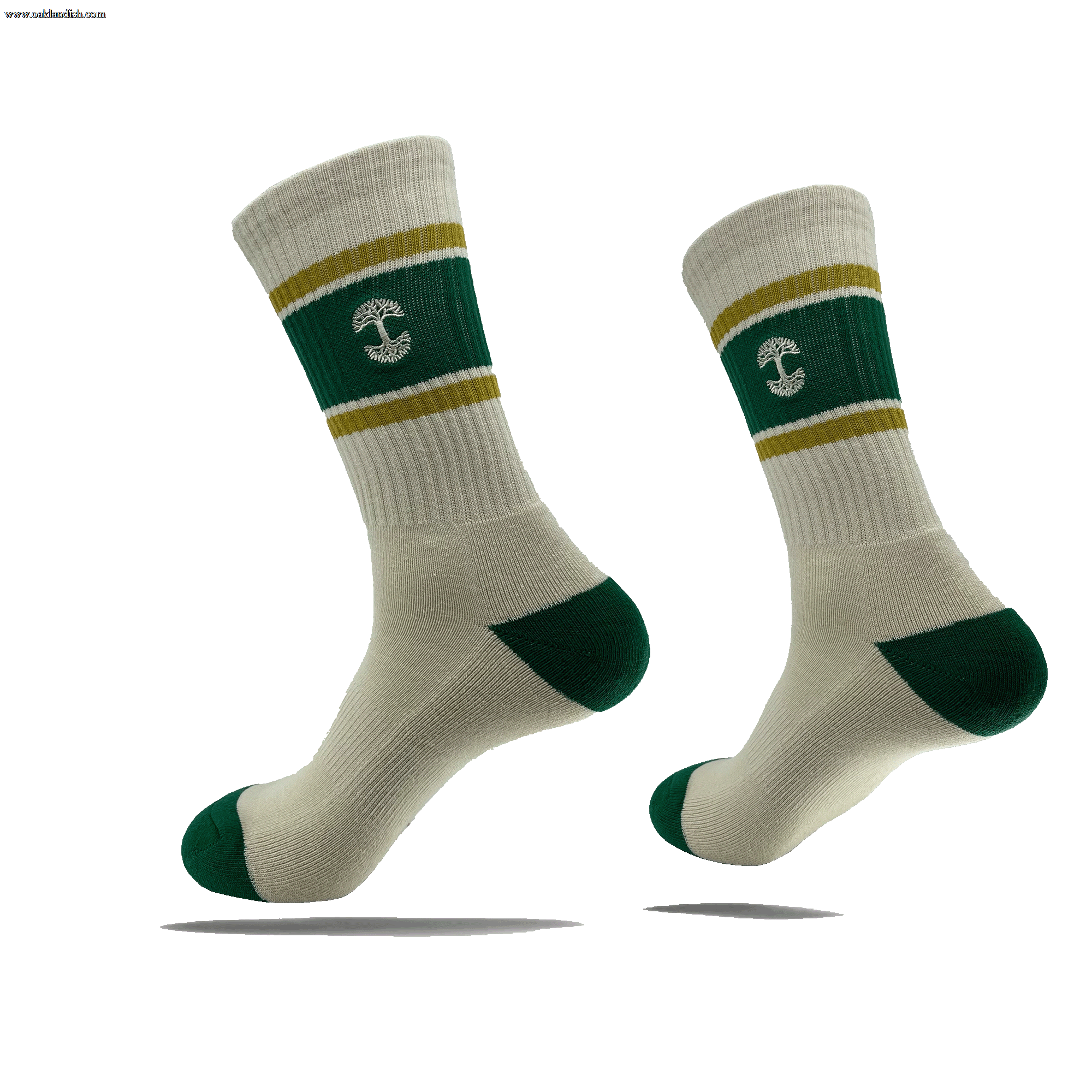 Introducing the Striped Classic Sock by Oaklandish: a pair of beige crew socks featuring green heels, toes, and cuffs. The socks sport a green band around the lower leg area, accented with two thin yellow stripes above and below it. At the center of this green band is a white anchor symbol. Crafted from 70% cotton, these stylish socks are available in adult sizes. They are showcased suspended in mid-air against a plain green background.
