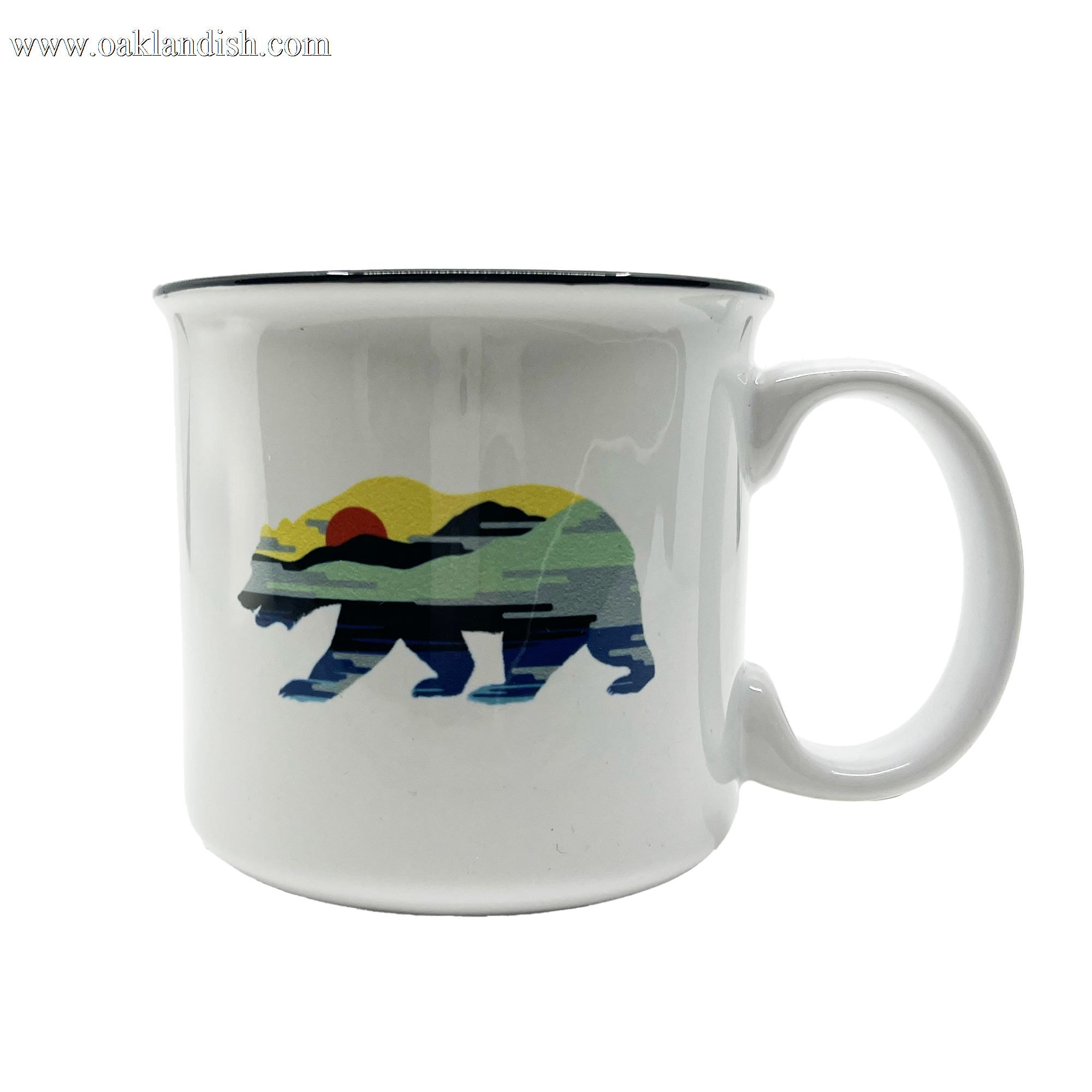 The Sunset Bear Coffee Mug by Oaklandish is a white ceramic mug with a thick black rim, showcasing a graphic of a California grizzly bear filled with a landscape design. The design features a serene outdoor scene with layers of hills and water bathed in the colors of a colorful sunset, including shades of green, yellow, orange, and blue.