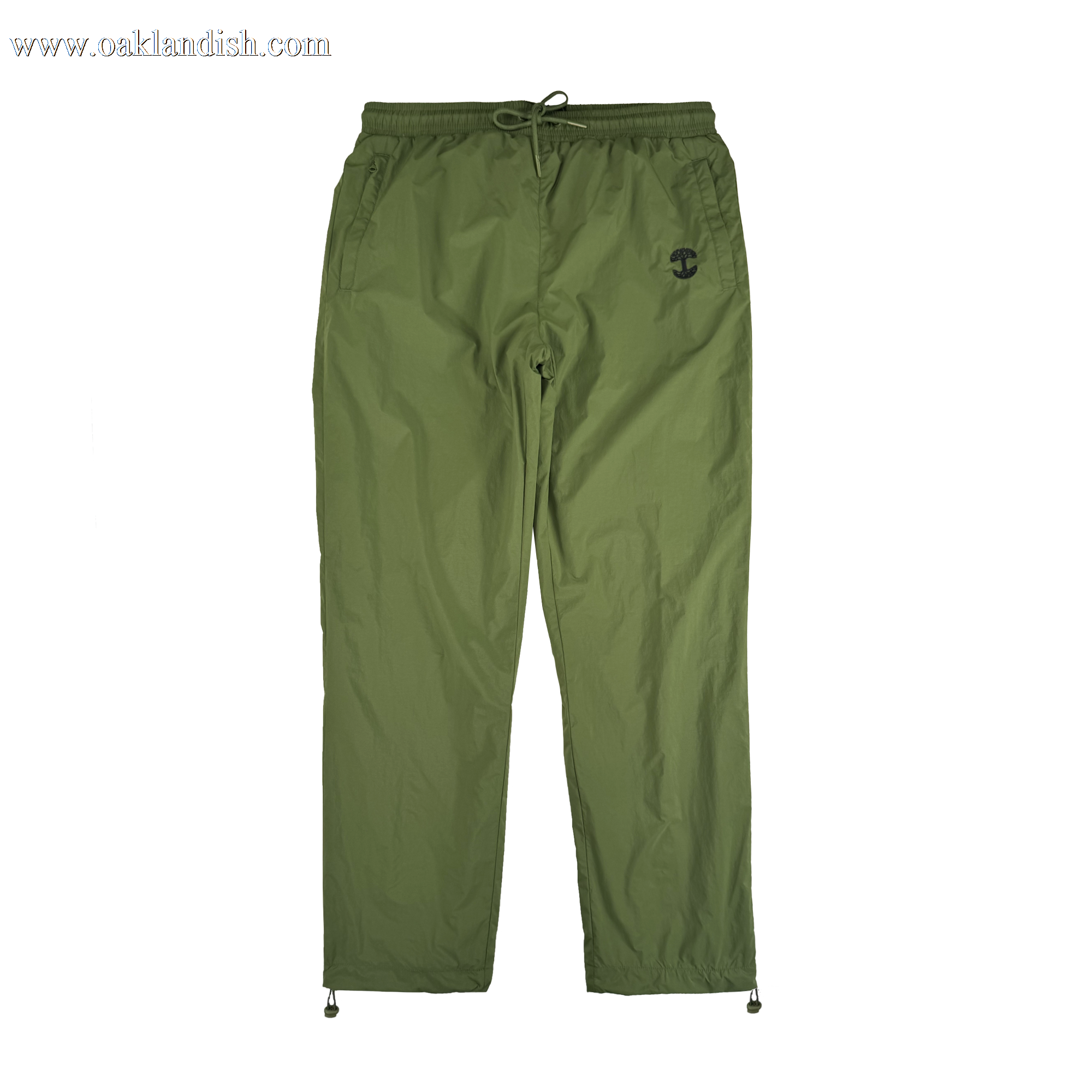 The Oaklandish Susurrus Track Bottom is an olive green jogger-style nylon pant with an adjustable waistband, drawstring closure, side pockets, ankle drawstrings, and a black army-inspired logo on the upper left thigh. Laid flat on a white background.