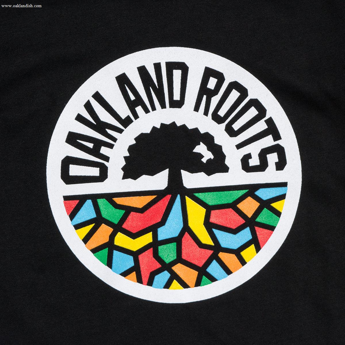 The Toddler Oakland Roots SC Classic Tee showcases the emblem of the Oakland Roots sports club. The design includes a black tree with roots extending downward, creating vibrant geometric shapes in red, yellow, blue, and green. The logo is enclosed within a white circle with "OAKLAND ROOTS" written in bold black letters around the top—ideal for a toddler t-shirt by Oakland Roots SC.